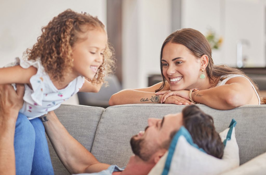 mom kid father playing sofa lounge family home colombia love care quality time together smile parents excited laughing child relax living room fun happiness joy web